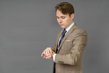 Saatine bakıp omzunun üstünde ceket tutan bir iş adamının portresi. Gri arka plan. İş ve finans kavramı