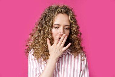 Genç ve güzel bir kadın eliyle yüzünü kapatıyor. Şaşırmış görünüyorsun. İzole edilmiş pembe arkaplan