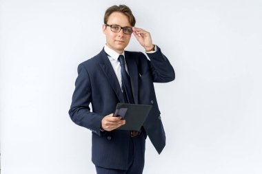 Mavi takım elbiseli bir iş adamının portresi elinde bir tablet tutuyor ve gözlüklerini ayarlıyor. Beyaz arka plan. İş ve finans kavramı