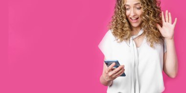 Genç bir kadın video bağlantısıyla telefonla iletişim kuruyor, duygularını ifade ediyor. Kadın portresi. Pembe arka planda izole edilmiş