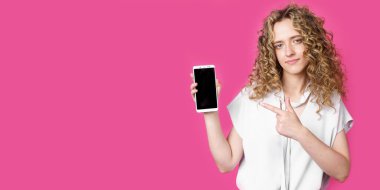 Şu cep telefonuna bak. Mutlu bir kadın işaret parmağını boş bir ekrana doğrultuyor ve modern bir cihaz gösteriyor. Pembe arka planda izole edilmiş. Teknoloji konsepti
