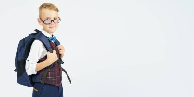 Okullu bir çocuk okul çantasını tutuyor, yan yana duruyor ve kameraya bakıyor. Eğitim kavramı