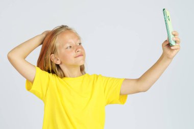 Sarı tişörtlü genç bir kız cep telefonundan selfie çekiyor. İzole edilmiş arka plan. Eğitim kavramı.