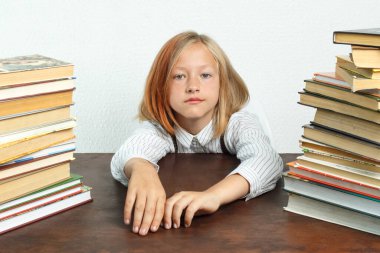 Kitapların arasında bir masada oturan genç bir kızın portresi. Kameraya bakıyor. İzole edilmiş arka plan. Eğitim kavramı.
