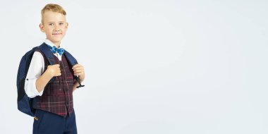 Okullu bir çocuk okul çantasını tutuyor, yan yana duruyor ve kameraya bakıyor. Eğitim kavramı