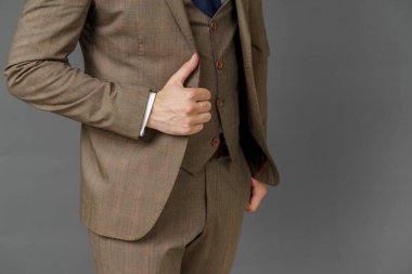 Takım elbiseli bir iş adamının portresi, elini ceketinin kenarından tutuyor. Görünürde yüz yok. Gri arka plan. İş ve finans kavramı