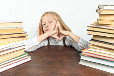 Kitapların arasında yorgun bir şekilde masada oturan genç bir kızın portresi. Avuçları önünde kıvrılmış. Eğitim kavramı.