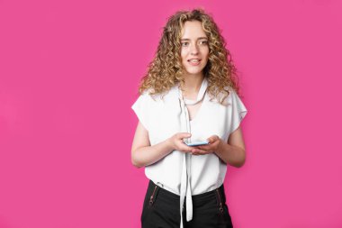 Genç bir kadın cep telefonunu elinde tutuyor ve gülümsüyor. İzole edilmiş pembe arkaplan