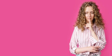 Genç bir kadın ellerini sessizce hareket ettiriyor ve dudaklarına uyguluyor. Pembe arka planda izole edilmiş