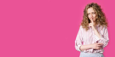 Genç bir kadın ellerini sessizce hareket ettiriyor ve dudaklarına uyguluyor. Pembe arka planda izole edilmiş