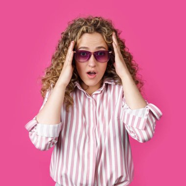 Genç bir kadın elleriyle başını tutuyor, şaşırıyor. Pembe arka planda izole edilmiş