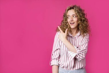 Genç ve güzel bir kadın parmağını sola doğru gösteriyor. İzole edilmiş pembe arkaplan