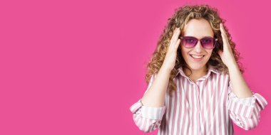 Genç bir kadın ellerini neşe ve sevinçle tutuyor. Pembe arka planda izole edilmiş