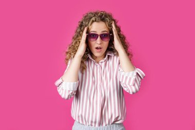 Genç bir kadın elleriyle başını tutuyor, şaşırıyor. Pembe arka planda izole edilmiş