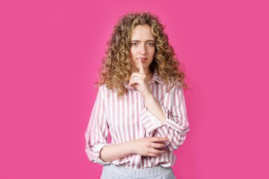 Genç bir kadın ellerini sessizce hareket ettiriyor ve dudaklarına uyguluyor. Pembe arka planda izole edilmiş