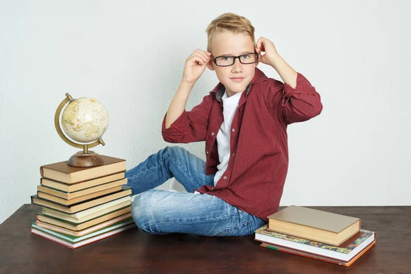 一个男孩坐在靠近书本和地球仪的桌子上 直着眼镜 教育概念 — 图库照片