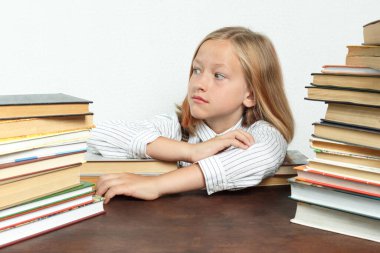 Kitapların arasında bir masada oturan ve yan tarafa bakan genç bir kızın portresi. İzole edilmiş arka plan. Eğitim kavramı.