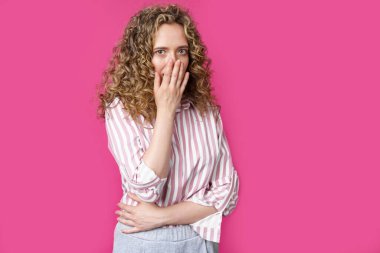 Genç ve güzel bir kadın eliyle yüzünü kapatıyor. Şaşırmış görünüyorsun. İzole edilmiş pembe arkaplan