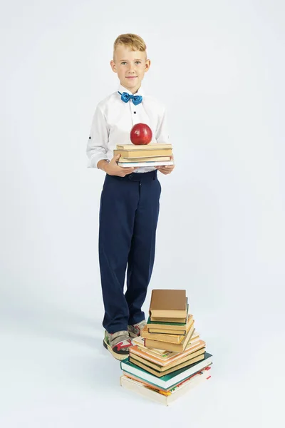 少年は本の山の近くに立ち 本とリンゴを手にしている 孤立した背景 教育理念 — ストック写真