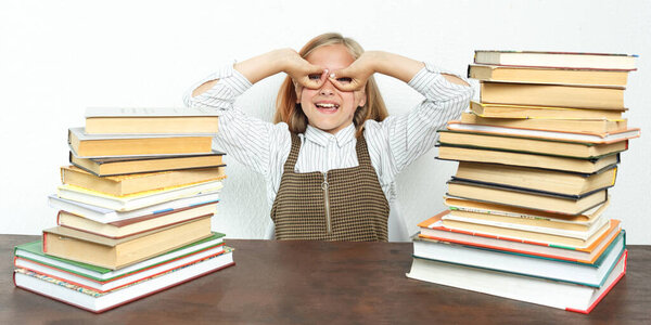 A portrait of a teenage girl sitting at a table among books depicts Batman. Education concept.