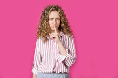 Genç bir kadın ellerini sessizce hareket ettiriyor ve dudaklarına uyguluyor. Pembe arka planda izole edilmiş