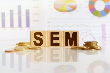Arama motoru pazarlama. SEM sözcüğü ahşap küplerle ilgili, küpler yansıtıcı yüzeyde duruyor, arka planda bir iş diyagramı var. İş ve finans kavramı