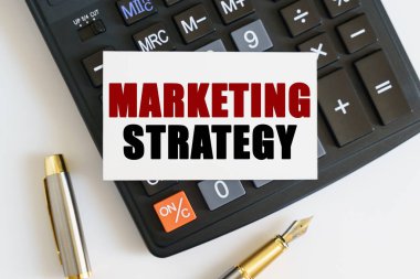 İş ve finans kavramı. Masanın üzerinde bir kalem, bir hesap makinesi ve metnin yazıldığı bir kartvizit var - MARKETING STRATEGY