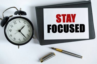 İş ve olumlu kavram. Masanın üzerinde bir saat, bir kalem, bir defter ve üzerine metin yazılmış bir kart var.