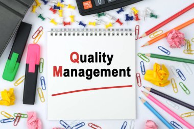 İş konsepti. Masanın üzerinde bir hesap makinesi, günlük, işaretleyiciler, kalemler ve üzerinde yazı olan bir defter - Kalite Yönetimi