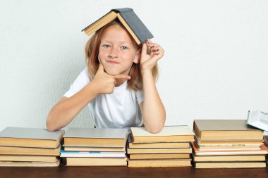 Eğitim konsepti. Bir öğrenci bir masada oturuyor ve kafası ders kitabıyla başının üzerinde dinleniyor. Kitaplar yakınlarda.