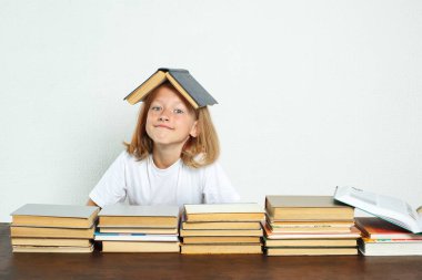 Eğitim konsepti. Öğrenci kafasında bir ders kitabı ile masada oturuyor. Kitaplar yakınlarda.