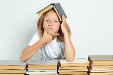 Eğitim konsepti. Bir öğrenci bir masada oturuyor ve kafası ders kitabıyla başının üzerinde dinleniyor. Kitaplar yakınlarda.