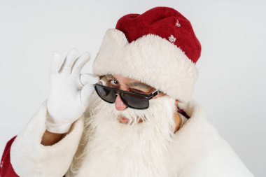 Tatiller ve Noel konsepti. Noel Baba gözlüğünü eliyle ayarlar. Beyazda izole edilmiş