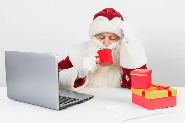 크리스마스와 새해의 개념이다 산타클로스는 책상에 앉아서 커피를 마시고 컴퓨터에서 일하고 — 스톡 사진