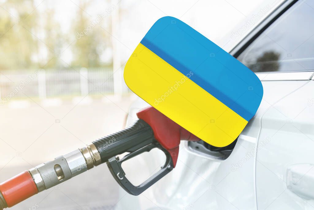 Energy and economy concept. Flag of Ukraine on the car's fuel filler flap with gas pump nozzle in the tank.
