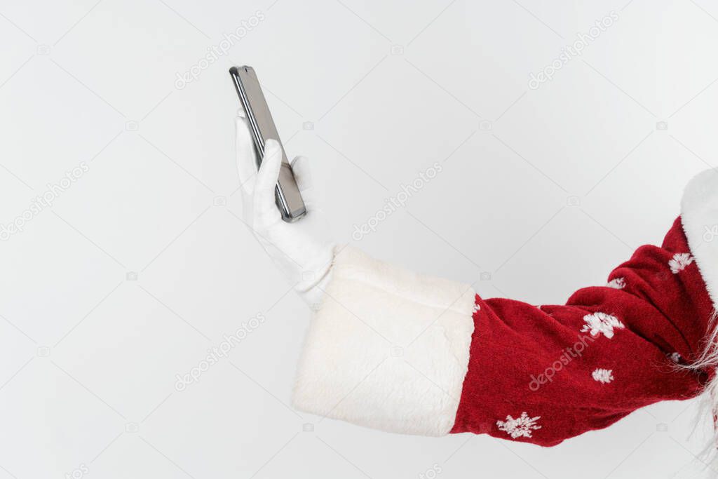 Christmas and New Years concept. Santa Claus holds a mobile phone in his hand. No face visible. Isolated background