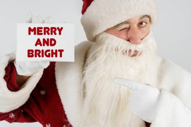 Yeni yıl ve Noel konsepti. Noel Baba elinde elinde bir kart tutuyor, neşeli ve parlak.