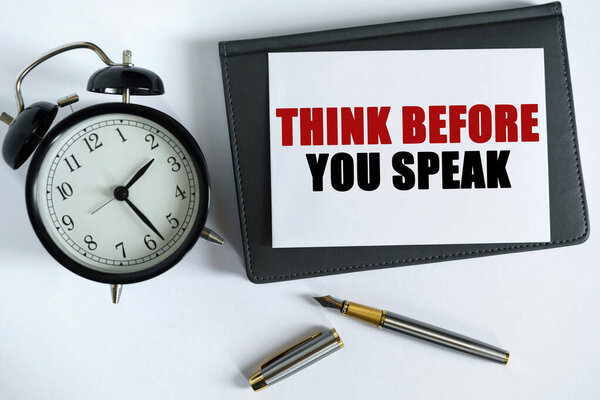 Бизнес и позитивная концепция. На столе есть часы, ручка, блокнот и карточка, на которой написан текст - подумайте прежде, чем вы заговорите