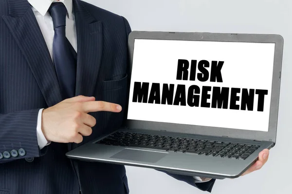 Finance and economics concept. A businessman holds a laptop in his hands and shows on the screen with the text - RISK MANAGEMENT