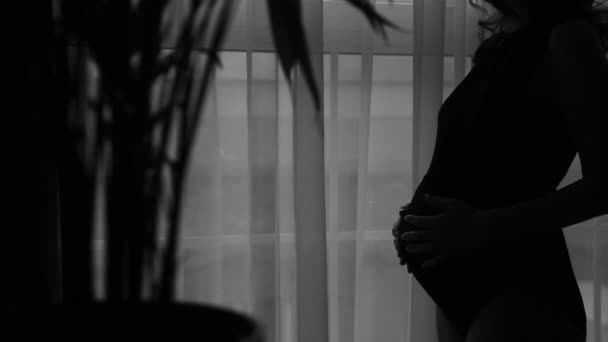 Těhotná žena v černém obleku a hladil ji po okně, — Stock video