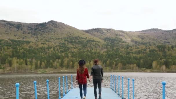 Hombre y mujer caminan por el muelle tomados de la mano cerca del río y las montañas — Vídeos de Stock