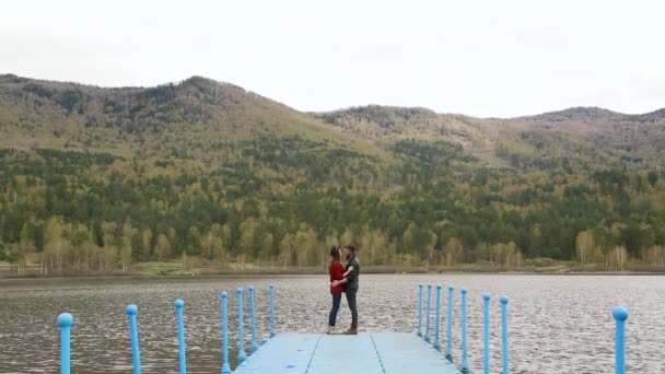 Мужчина подбирает женщину на пирсе у реки и горы — стоковое видео