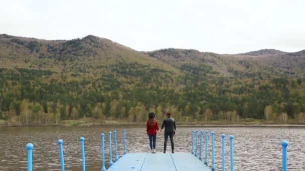 Flicka kramar en man på piren nära floden och bergen på sommaren — Stockvideo