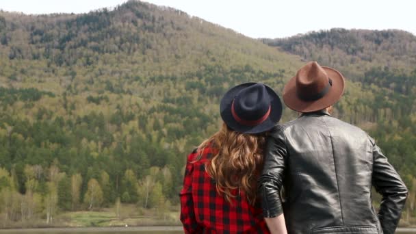 Un hombre abraza a una chica. cerca de montañas y ríos. Verano en sombreros — Vídeos de Stock