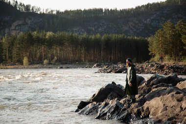 adam sakal bıyık yağmurluk bir kova ile bir nehir yakınında duruyor