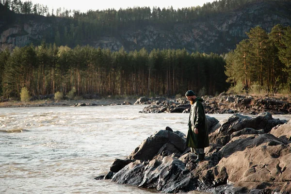 man beard mustache raincoat is standing near a river with a bucket