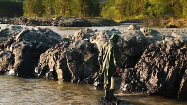 Man Beard mustasch regnrock står nära en flod med en hink — Stockvideo