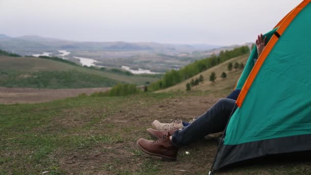 Man and woman peeking out of a green tent with on top of a mountain — Stock Video