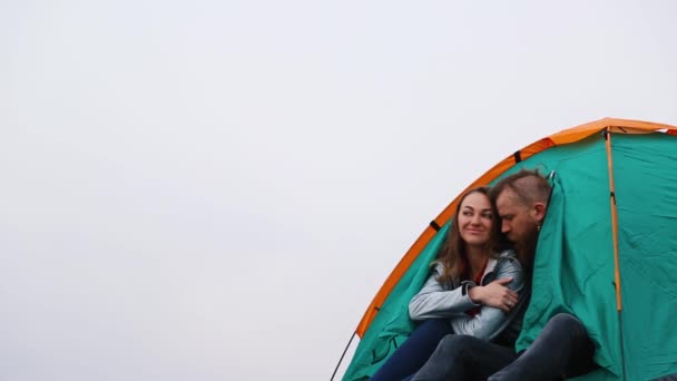 Мужчина и женщина, выглядывающие из зеленой палатки на вершине горы — стоковое видео