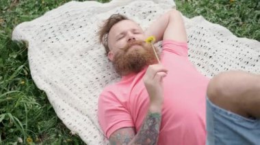 Erkek çimenlerin üzerinde sarı çiçekle yatar, pembe tişört yazın güzel havanın tadını çıkarır.